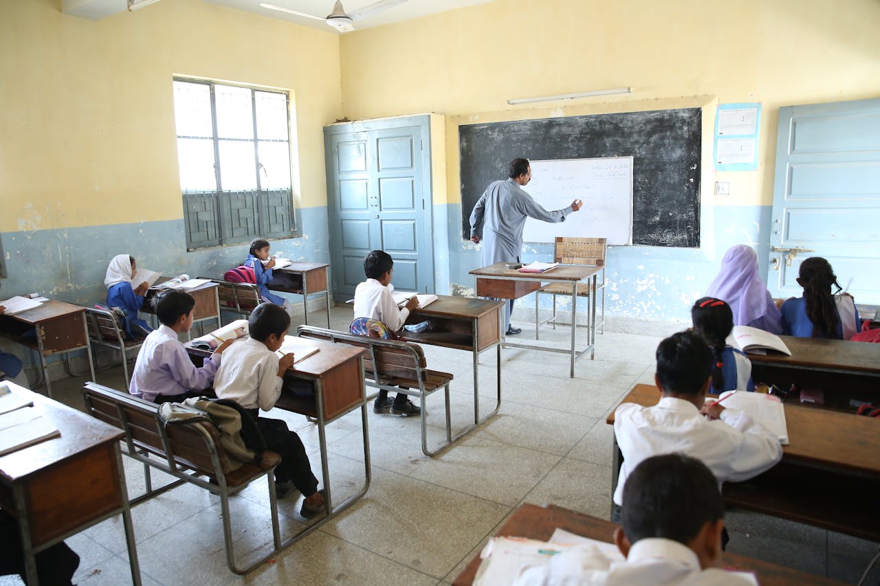 portfolio-03 Elementary classroom with attentive students and teacher at blackboard, promoting education.